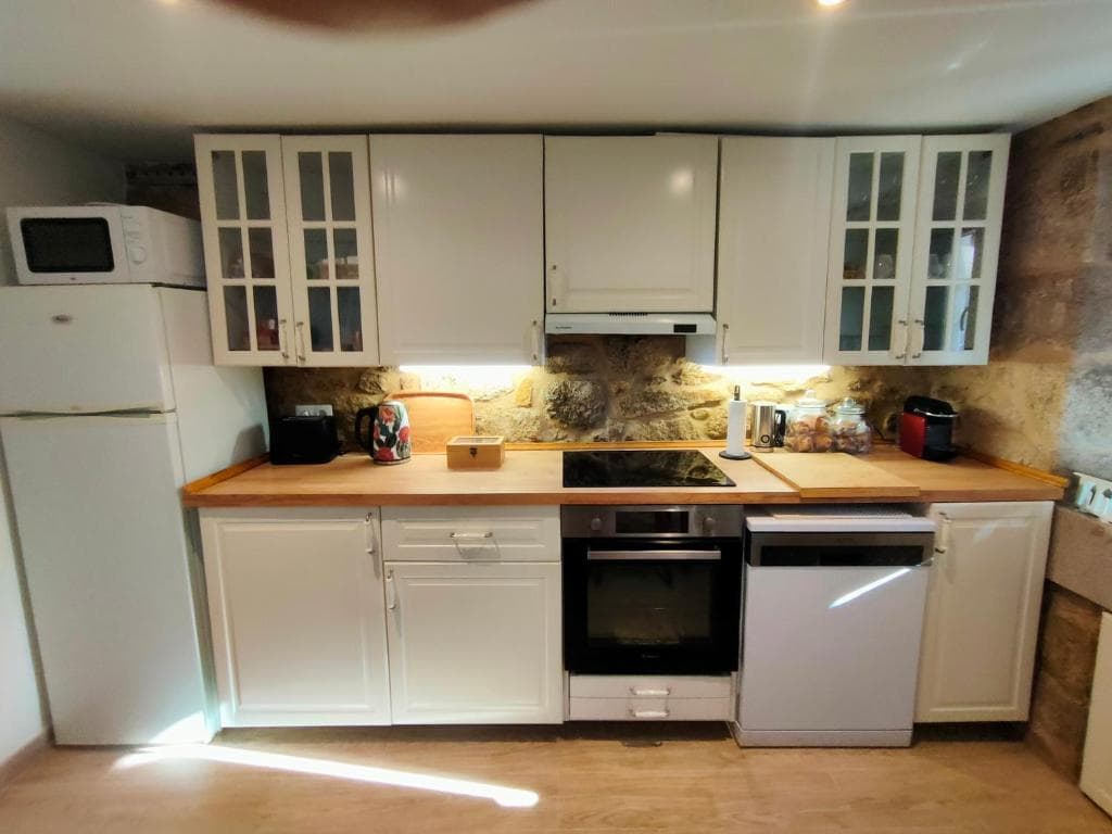 Cocina equipada con muebles blancos y muro de piedra